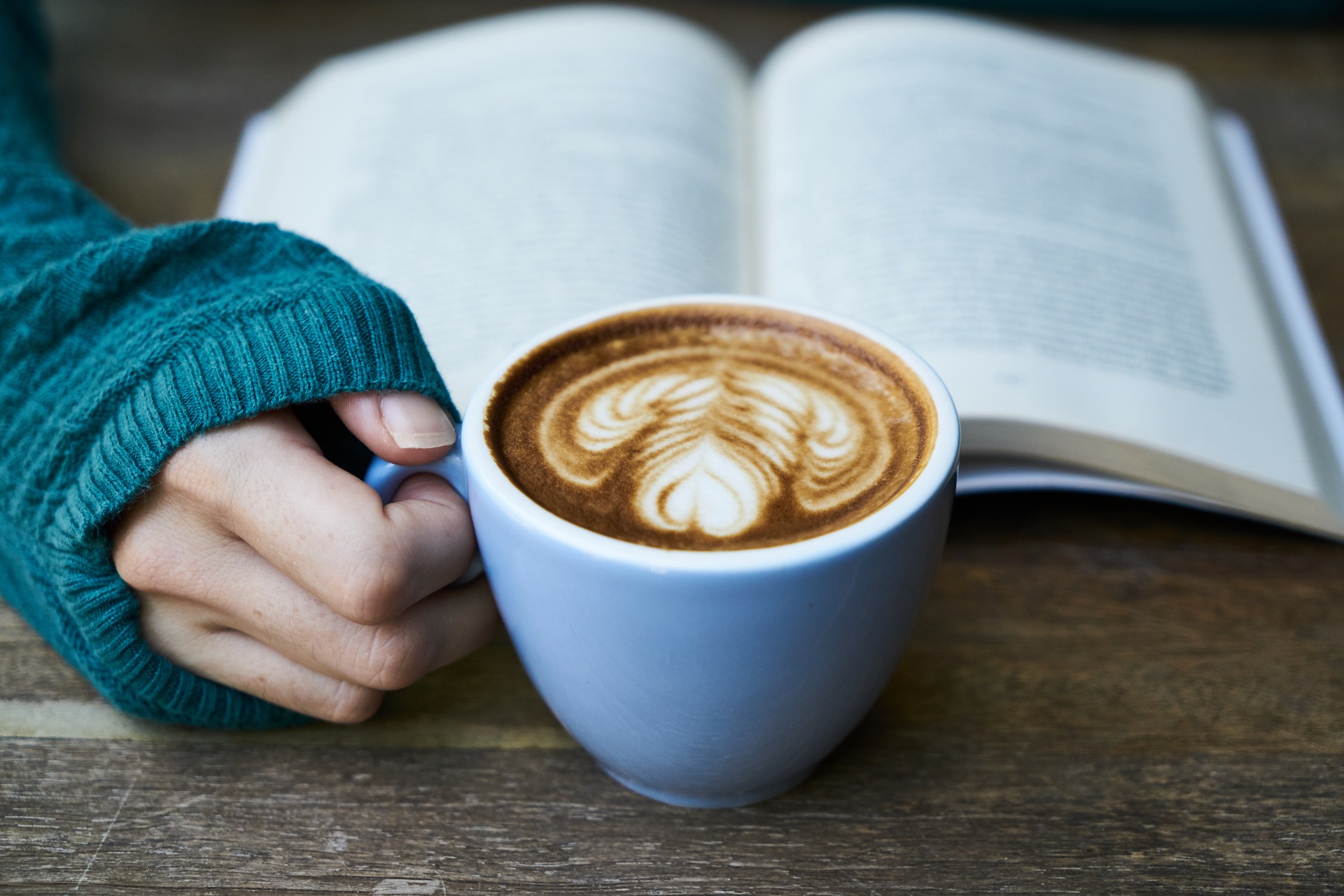 Mano sosteniendo una taza de café delante de un libro.