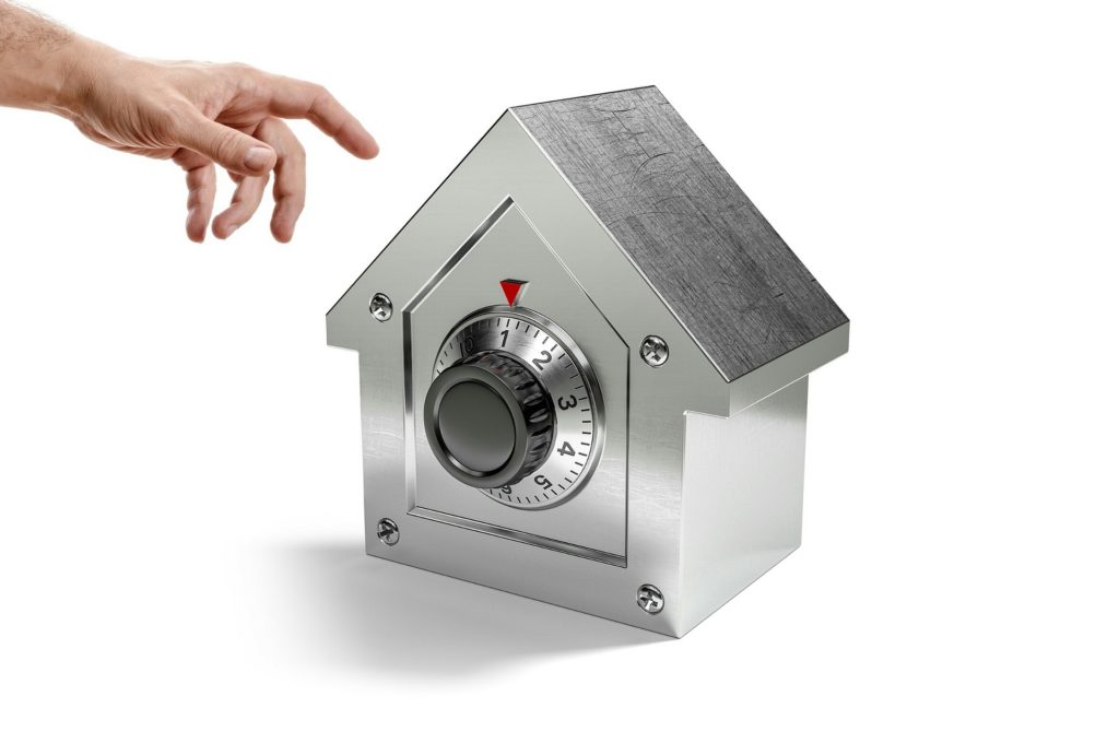 Metal house-shaped safe with a large combination lock. A hand is reaching for the house.