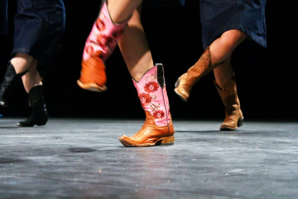Three sets of legs with cowboy boots on, mid-dance step.