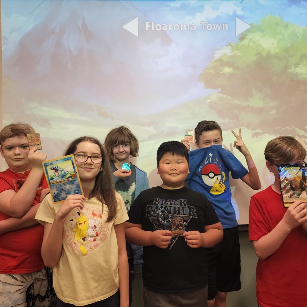 Happy kids holding up Pokémon themed items in front of a Pokémon themed background.