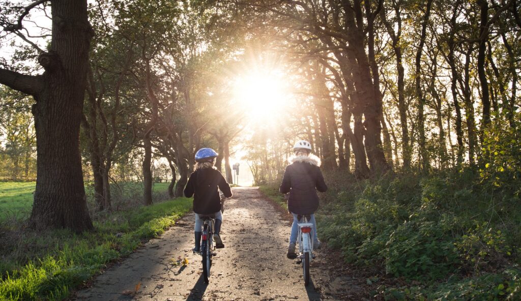 Two girls on a bike in the woods, riding towatd the sun.